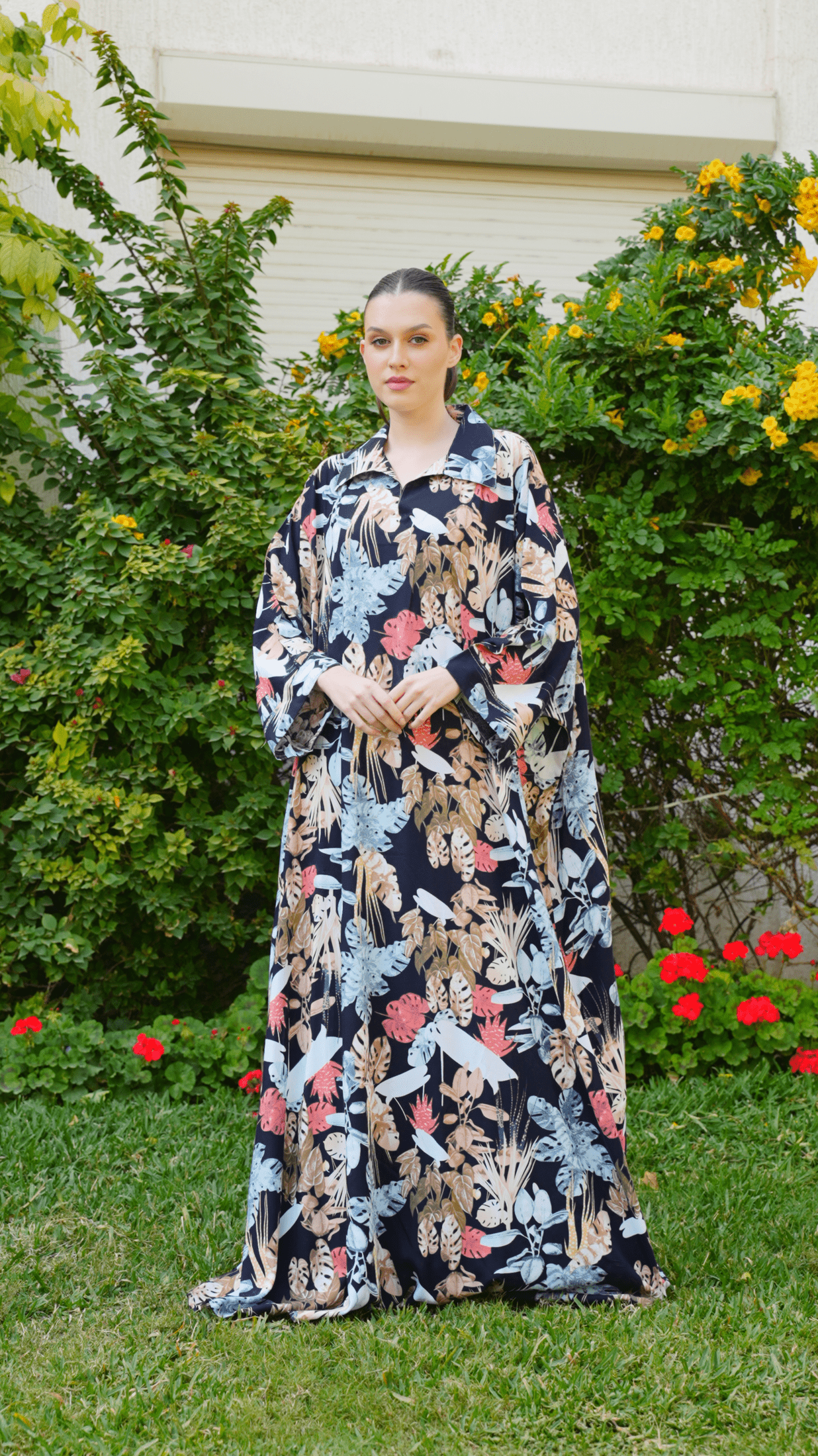 Woman in a floral dress standing outdoors with greenery and flowers in the background