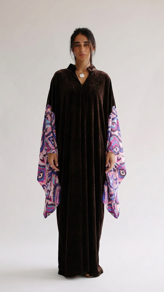 Woman wearing a long dark brown dress with colorful sleeves against a white background